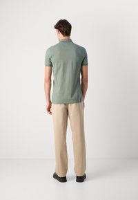 Lys grønn kortermet polo-shirt med teksturert overflate, sammen med løse beige bukser og svarte sko, sett fra baksiden.