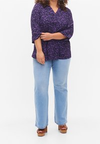 Blouse à imprimé léopard violet avec col en V, manches trois-quarts et coupe décontractée, associée à un jean bleu clair à jambes droites et des chaussures compensées marron.