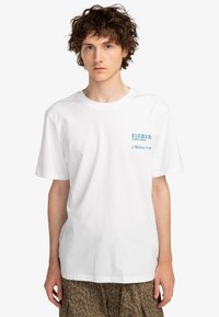 Bílý bavlněný tričko s krátkým rukávem, na levé části hrudi s modrým nápisem "ELEMENT 75000 PARIS L'Addition SVP". Jednoduchý design.