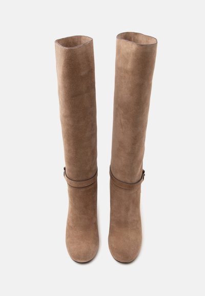 Paire de bottes hautes en suède marron avec bouts arrondis et lanières décoratives autour de la cheville, présentées debout.