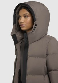 Kergedusjakke heled pruunis, suure kapuutsiga, ees luku ja mustade detailidega. Omab tikandimustreid ja mugavat istuvust.