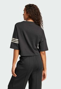 Čierne skrátené tričko s krátkymi rukávmi, ktoré má na každom rukáve tri biele pruhy a hladkú bavlnenú textúru.