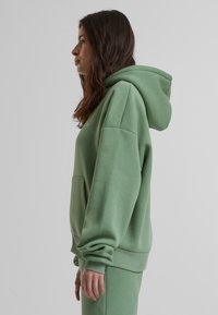 Sweatshirt à capuche verte, en mélange de coton doux, avec une poche kangourou, des poignets côtelés et une coupe décontractée.