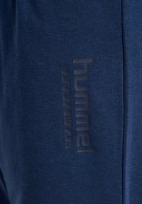 Pantalon de sport bleu marine en tissu texturé, avec un logo en caoutchouc positionné verticalement le long du côté.