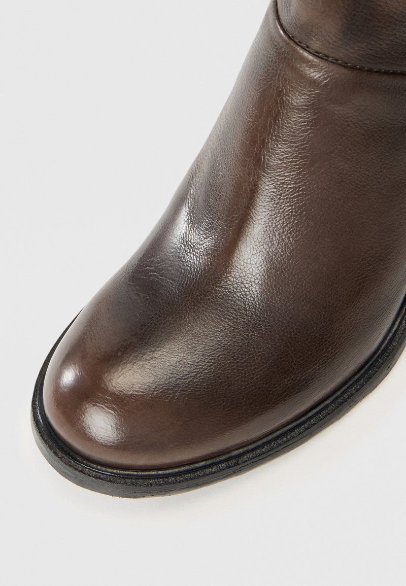 Stivale alla caviglia in pelle marrone con punta arrotondata, texture liscia, suola nera e dettagli di cucitura minima lungo il bordo.