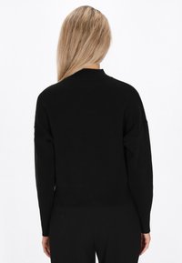 Pulover din tricot negru cu guler �înalt, margine cu nervuri și mâneci lungi, având o textură netedă fără modele vizibile sau detalii din metal.