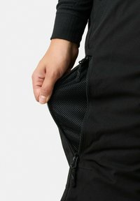 Zwarte sportbroek met een ritszakje aan de zijkant die een meshvoering toont. De stof lijkt glad, met een aansluitend ontwerp en geribbelde boorden.