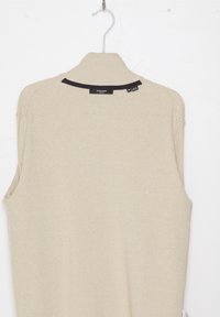 Beige ärmlös ribbad tröja med hög krage, med en mörk detalj längs halsringningen och etiketter på baksidan.