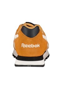 Zapatillas Reebok en ante naranja con detalles en blanco, presentan una pestaña en el talón negra y un logo blanco en la parte trasera, diseño ligero, superficie texturizada.