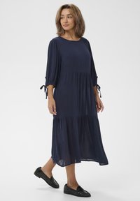 Marineblaue Midi-Kleid mit Dreiviertelärmeln, gerafftem Oberteil und Kordelzugdetails an den Ärmeln. Leichter Stoff mit lockerer Passform.