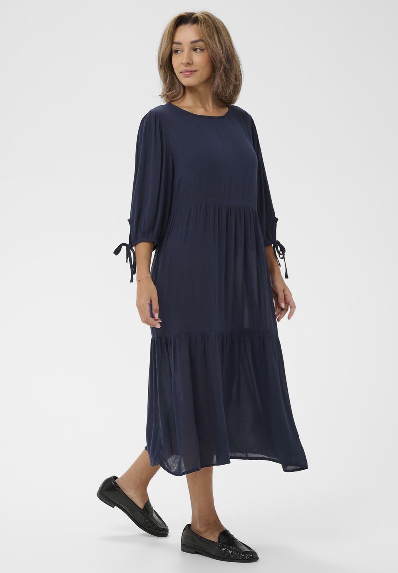 Marineblaue Midi-Kleid mit Dreiviertelärmeln, gerafftem Oberteil und Kordelzugdetails an den Ärmeln. Leichter Stoff mit lockerer Passform.