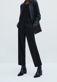 Zwarte op maat gemaakte blazer over een zwarte top, gecombineerd met hoog-gewijde zwarte trousers en enkellaarsjes. Gladde textuur, gestructureerde pasvorm, strakke ontwerp.