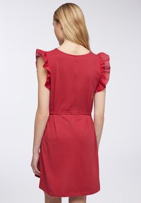 Abito rosso con maniche corte a volant, vita stretta e texture liscia. La vista posteriore mostra un collo rotondo e una lunghezza sopra il ginocchio.