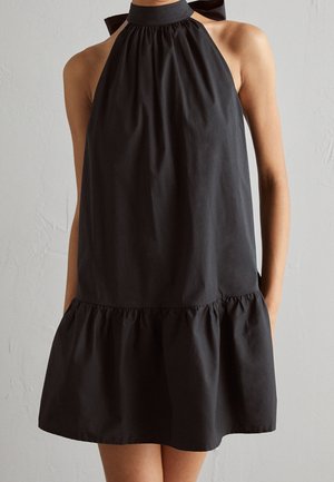 Czarna sukienka na halter z marszczonym dekoltem i ozdobną kokardą. Posiada falbaniaste, warstwowe wykończenie i gładką tkaninę o luźnym kroju.