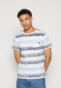 Camiseta a rayas en blanco, azul y marino. Presenta un cuello redondo, mangas cortas y un pequeño bolsillo en el pecho. Está hecha de una tela texturizada.