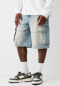 Džínové cargo šortky světle modré barvy, s mnoha kapsami, volným střihem a vybledlou texturou. V kombinaci s tmavými teniskami a bílými ponožkami.