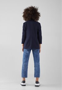 Mörkblå blazer med skräddarsydd passform, matchad med ljusblå jeans och svartvita sneakers. Slät tyg med synliga söm detaljer.