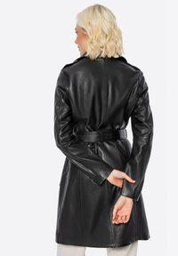 Cappotto in pelle nera con vita a cintura, maniche lunghe e texture morbida, progettato con colletto classico e vestibilità aderente.