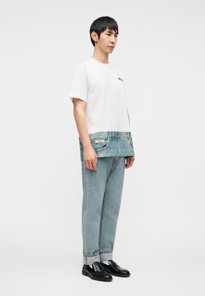 Λευκό T-shirt με κοντά μανίκια και κάτω μέρος που μοιάζει με τζιν, με τσέπες και ετικέτα. Συνδυάζεται με ανοιχτό μπλε τζιν και μαύρα παπούτσια.