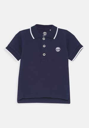 Polo azul marino de manga corta con ribete blanco en el cuello y las mangas, tres botones y un logo de árbol blanco en el pecho.