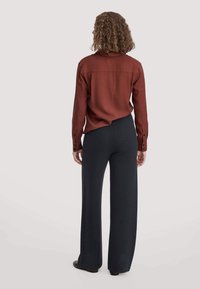 Rostfarbige Bluse mit Kragen und Rückenpasse, kombiniert mit schwarzen weit geschnittenen Hosen. Beide Kleidungsstücke haben eine glatte, weiche Textur.
