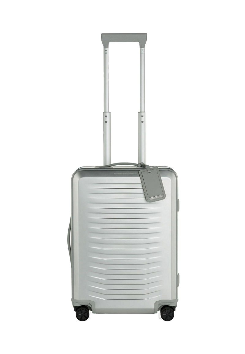 Maleta rígida plateada con ranuras horizontales, doble asa telescópica, cuatro ruedas negras y una etiqueta de equipaje desmontable.
