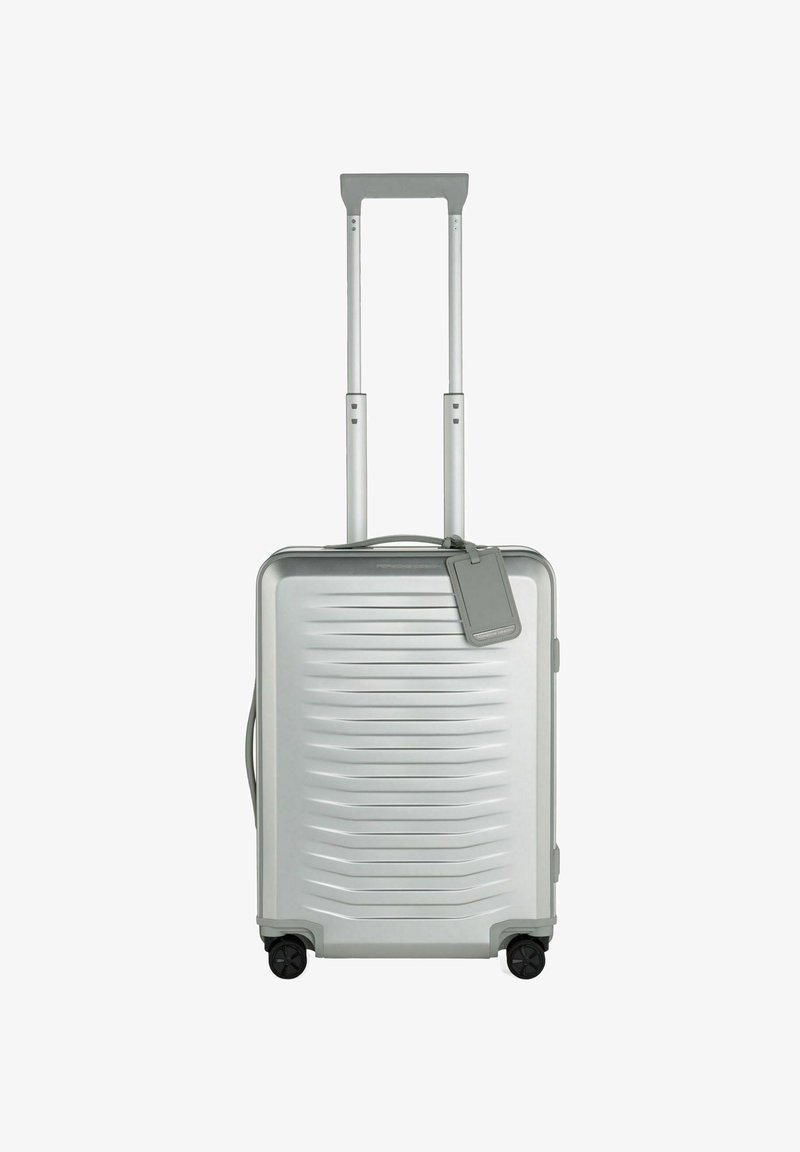 Maleta rígida plateada con ranuras horizontales, doble asa telescópica, cuatro ruedas negras y una etiqueta de equipaje desmontable.
