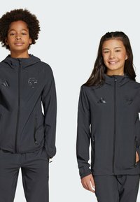 Vestes noires zippées faisant partie des vêtements de sport, avec capuche, poches zippées et logo brodé. Fabriquées en tissu léger et lisse.
