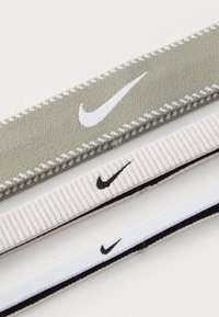 Tre Nike hårbånd: et olivengrønt med hvid syning, et lys rosa ribbet, og et sort-hvid stribet design.