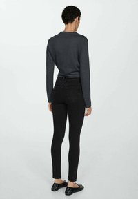 Camisa de manga larga gris oscuro combinada con jeans skinny negros. El conjunto presenta un diseño ajustado y una textura de tela suave. Unos zapatos planos negros completan el look.