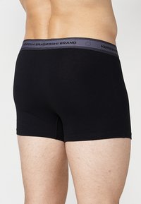 Fekete bokszernadrág sima anyagból, szürke elasztikus derékpánttal, amelyen a "KOROSHI BRAND" felirat dombornyomott.