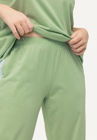 Ljust gröna bomullsbukser med elastisk midja, som har en avslappnad passform och mjuk textur, delvis täckta av en lös matchande topp.