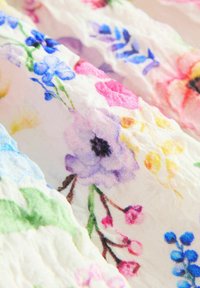 Witte stof met een gerimpelde textuur met kleurrijke bloemmotieven in blauw, roze, paars, geel en groen.