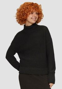Pull en tricot noir avec un col roulé haut, des épaules tombantes et des poignets côtelés. Surface texturée avec un design ample.
