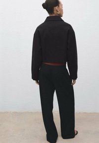 Giacca nera a croppet con colletto, abbinata a pantaloni neri a vita alta e gamba larga. Design semplice, colori uni, nessun motivo visibile.
