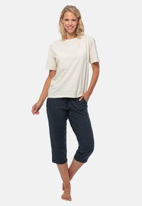 Beige bomullströja i kombination med marinblå utsvängda byxor med vita prickar. Outfiten har en avslappnad passform och en ledig design.