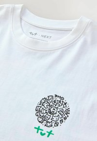 Hvid bomulds t-shirt med en cirkulær sort grafik med forskellige doodles og et grønt "+" symbol under designet.