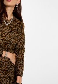 Luipaardprint trui in bruin en zwart, met lange mouwen. Accessoires met een zilveren kettinghalsband en een gestructureerde armband.