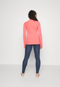 Langermet, tettsittende topp i lys rosa, kombinert med høyt liv navy leggings; glatt tekstur, elastisk materiale, atletisk design.