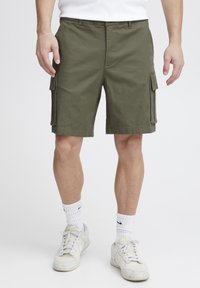Olivenfarvede cargo-shorts lavet af bomuld, med sidelommer, en afslappet pasform og lige ben. Båret med hvide sneakers og sokker.