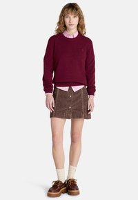 Burgundy tröja över en rosa skjorta med krage, tillsammans med en brun kordflorskjol med framknappar och bruna platåskor med krämfärgade strumpor.