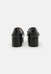 Pantofi platform din piele neagră cu o textură netedă, vârf rotunjit și detaliu cu cataramă. Tocuri masive oferă înălțime. Vedere din spate.