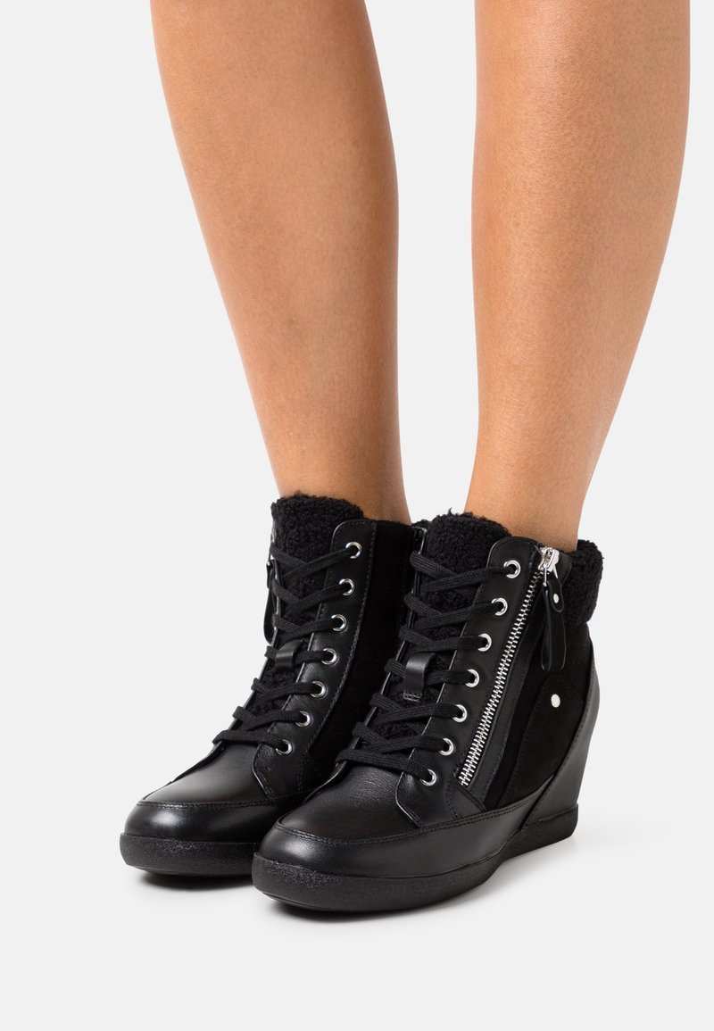 Black high-top wedge sneakers with a smooth leather exterior, textured fleece collar, and side zipper detail. Features lace-up front.