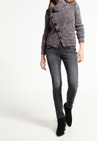 Gebreide trui in paarse en grijze tinten met een losse col en zwarte knopen; gecombineerd met slim-fit grijze jeans en zwarte enkellaarsjes.