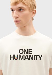 Weißes Baumwoll-T-Shirt mit fett gedrucktem schwarzen Text "EINE MENSCHHEIT" und bunten Punkten auf dem Buchstaben "U." Kurze Ärmel und runder Halsausschnitt.