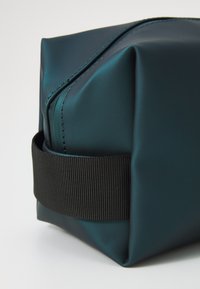 Teal vanntett toalettveske med rektangulær form, med et svart elastisk bånd og en glatt, blank overflate.