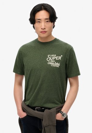 Grøn meleret bomulds T-shirt med et hvidt trykt logo, rund halsudskæring og korte ærmer, parret med mørk denim og et brunt bælte.
