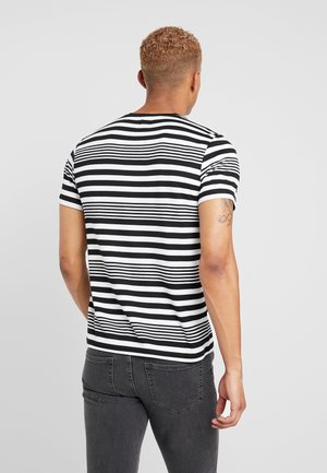 Czarnobiała koszulka w paski z krótkim rękawem, okrągłym dekoltem i dopasowanym krojem, noszona z ciemnymi dżinsami, widziana od tyłu.