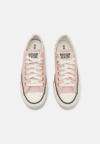 Pink canvas sneakers with white laces, gold eyelets, and a rubber sole. Features black strip and All Star logo on the tongue. Size 8.