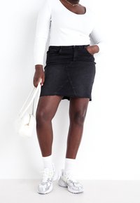 Černá džínová minisukně s ragged lemem a předním švem, v kombinaci s bílým dlouhým rukávem a šedými běžeckými botami. Bílá crossbody taška.